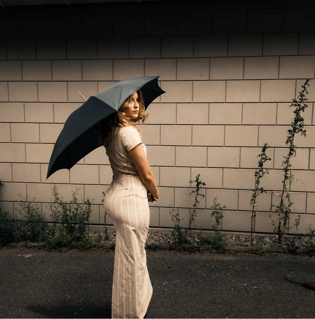 Model im hellen Rippenkleid mit schwarzem Regenschirm